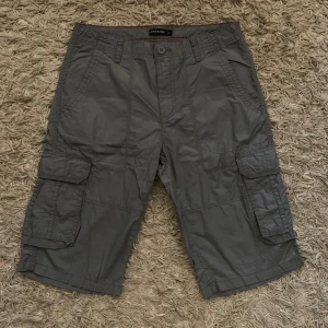 Grå cargoshorts från LCW Casual - Säljer ett par grå cargoshorts från LCW Casual med flera praktiska fickor på sidorna och bak. Shortsen har normal passform och är perfekta för sommaren. Stängs med knapp och dragkedja. Klassisk och stilren design.