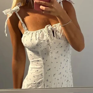Vit sommarklänning med blommigt mönster och knytband - Superfin vit klänning med små blommor och knytband på axlarna. Nakd men säljs ej längre! Skickar såklart gena bilder, går en bit under knäna! 