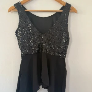 Svart paljetttröja från Sisters Point - Snygg svart tröja/topp från Sisters Point med paljetter upptill och ärmlös design. Nederdelen är i ett lätt, flödande tyg som ger en festlig känsla. Perfekt för dig som vill sticka ut med lite extra glitter.