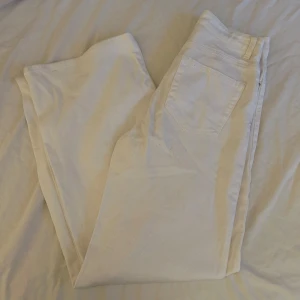 Vita vida jeans från H&M Divided - Säljer ett par vita jeans från H&M Divided i storlek 36. Byxorna har hög midja och vida ben, klassisk femficksmodell och stängs med knapp och dragkedja. Perfekta för en fräsch och stilren look.