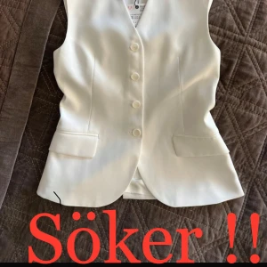 Vit väst från Zara med knappar - Stilren vit väst från Zara med v-ringning och knäppning framtill. Västen har två fickor fram och ett smalt bälte baktill för justerbar passform. Perfekt att styla över en skjorta eller t-shirt.