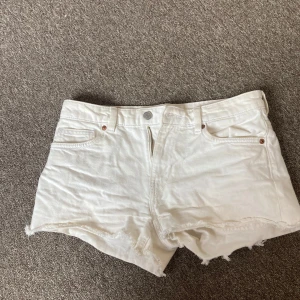 Vita jeansshorts från Monki - ✨Säljer ett par vita jeansshorts från Monki med midjemåttet 40cm. Klassisk femficksmodell med knapp och dragkedja framtill. Perfekta för varma dagar och enkel att matcha med olika toppar.✨