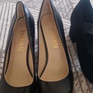 Svarta pumps från Samurai och mockaliknande ballerinaskor - Två par svarta damskor: ett par klassiska pumps i skinnimitation från Samurai med rund tå och ett par ballerinaskor i mockaliknande material med breda elastiska band över foten.