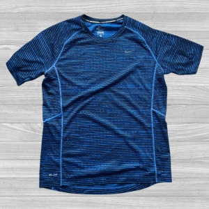 Nike running miler - Säljer en blå och svart randig Dri-Fit t-shirt från Nike. Perfekt för löpning eller träning, med ventilerande material och korta ärmar. Snygg sportig design med Nike-logga på bröstet och Dri-Fit-tryck nedtill.