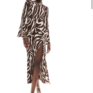 Brun och vit långklänning med zebramönster - Säljer en långklänning med zebramönster i brunt och vitt . Klänningen har lång ärm, rund halsringning och en hög slits framtill. Materialet är ribbat och stretchigt vilket ger en snygg passform. Klänningen går ner till fötterna på mig som är 167 cm!