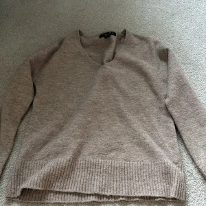 Beige stickad tröja från Amisu - Mysig beige stickad tröja från Amisu med v-ringad hals och ribbade muddar. Perfekt för lager-på-lager och passar till många olika outfits. Enkel och stilren design som är lätt att matcha.