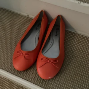 Orange ballerinaskor  - Säljer ett par orange ballerinaskor från Flexisole med rund tå och söt rosettdetalj framtill. Skorna har en platt sula och är perfekta för dig som vill ha något färgglatt och bekvämt till vardags. As snyggt till svarta jeans!! Säljer pga köpte fel stl!!