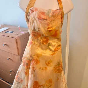 Halter Blommig klänning öppna ryggen  - Charmig blommig klänning i ljusa toner med snörning i ryggen. Klänningen har axelband . Perfekt för sommarens festlighet.          Klänning stl S men lite mindre som stl xs