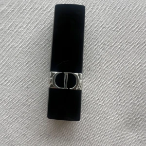 Rouge Dior 720 Icone Velvet läppstift - Säljer ett Rouge Dior läppstift i nyansen 720 Icone Velvet. Färgen är en djup, matt röd med sammetsfinish. Hylsan är svart med silverdetaljer och Dior-logga. Perfekt för dig som vill ha en klassisk och elegant look.  Kommer utan förpackning, oanvänd och otestad, om du köper fler av dessa läppstift kan jag tänka mig bättre pris. Rensning inför flytt. Vissa märken på själva skalet på läppstiftet kan förekomma då jag förvarat alla i samma låda 