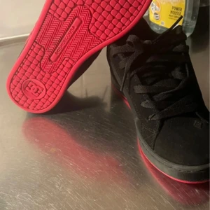 Svarta DC sneakers med rosa detaljer - Säljer ett par svarta DC sneakers med rosa detaljer och rosa sula. Skorna har snörning och är tillverkade i mocka med klassisk DC-logga på sidan. Perfekta för dig som gillar streetwear och skate-stil. 