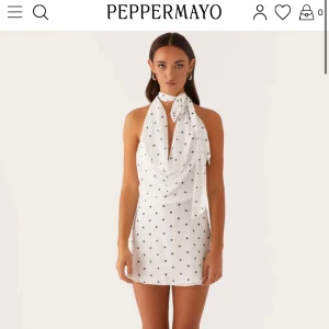 Vit prickig klänning PepperMayo - Supersöt kort vit klänning med svarta prickar från PepperMayo. Halterneck med knyt i nacken, draperad framsida och helt öppen rygg. Perfekt för sommarens alla tillfällen när du vill sticka ut lite extra. Den är helt ny och aldrig använd då den är för liten för mig, köpt för €69,95 = 780kr plus 150kr i frakt. Lappar osv sitter kvar.