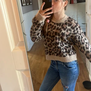 Beige leopardmönstrad stickad tröja - Säljer en supermjuk stickad tröja i beige med leopardmönster. Tröjan har rund halsringning, ribbade muddar och lång ärm. Perfekt för dig som vill ha en trendig och cozy look med lite edge.