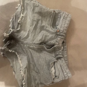 Grå jeansshorts - Snygga grå jeansshorts från Divided med råa fransade kanter och klassisk femficksdesign. Shortsen har bälteshällor, knapp och dragkedja framtill samt en loose fit. Perfekta för sommardagar när du vill ha en avslappnad och trendig look.
