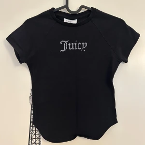 Svart topp med strass från Juicy Couture - Svart kortärmad topp med glittrande strassbokstäver som stavar 'Juicy' på bröstet från Juicy Couture i storlek XS. T-shirten har rund halsringning. Är i mycket bra skick. 