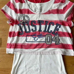 Randig t-shirt från Justice - Snygg kortärmad t-shirt från Justice med breda röda och vita ränder, tryck med texten 'Justice Est. 04' och nitar runt bokstäverna. T-shirten har rund halsringning och är i mjuk bomull. Perfekt för en avslappnad stil.