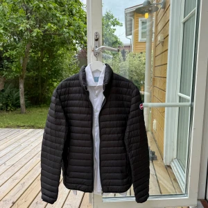 Svart dunjacka från Colmar - Säljer en svart, lätt och stilren dunjacka från Colmar. Jackan heter Colmar mens down Jacket, den är vindtålig och vattenavvisande - perfekt för vår/höst och sommarkvällar. Nyskick förutom dragkedjan som är lite trög. Du får med en vit skjorta från La chemise i storlek 39. 