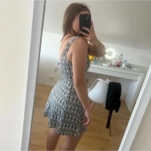  mönstrad kort klänning - Supersöt svartvit klänning med grafiskt mönster och ärmlös design. Klänningen har en rundad urringning och markerad midja som ger en snygg siluett. Perfekt för varma dagar i stranden och enkel att styla med smycken eller sneakers.