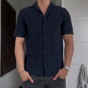 Mörkblå kortärmad skjorta från Zara - Snygg mörkblå skjorta från Zara i storlek S. Skjortan har korta ärmar, klassisk krage och knäppning framtill. Materialet är strukturerat och känns mjukt mot huden, perfekt för en avslappnad men stilren look.