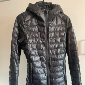 Svart Everest jacka - Säljer en svart dunjacka från Everest med huva. Jackan är quiltad och har en lätt glansig yta, perfekt för kyliga dagar. Klassisk passform och stilren look som funkar till det mesta.