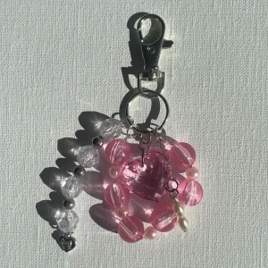 Rosa bag charm/nyckelring med hjärta - Supergullig väskberlock med stora rosa och klara pärlor, ett glittrigt rosa hjärta i mitten och små vita pärlor. Silverfärgad karbinhake och detaljer, samt en liten hjärtberlock längst ner. Perfekt accessoar för att pimpa din väska.