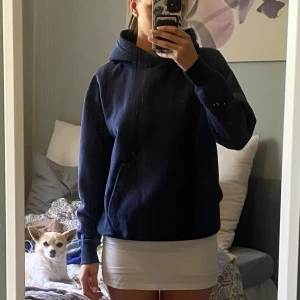 Mörkblå hoodie med huva - Enkel och stilren mörkblå hoodie med huva och känguruficka framtill. Tröjan har en loose passform och långa ärmar, perfekt för att slänga på sig när det är lite kyligare. 