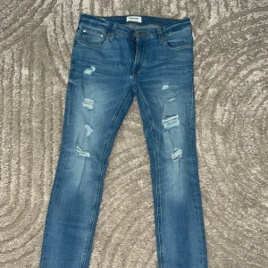 Blå skinny jeans Jack & Jones - Snygga blå skinny jeans från Jack & Jones, modell Liam. Jeansen har slitna detaljer och hål på benen för en trendig look. 