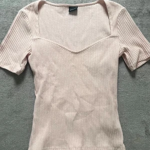 Ljusrosa ribbad topp från Gina Tricot -  ljusrosa ribbad topp från Gina Tricot med korta ärmar och v-ringad skärning. Toppen har en figurnära passform.