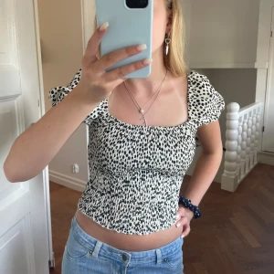Prickig croppad blus med puffärm - UPPSKATAD STORLEK, men kan kolla om nån är intresserad av storlek och märke!🩷Supersöt croppad blus med svartvita prickar och puffiga korta ärmar. Smockad överdel som sitter tajt men ändå stretchig. Fyrkantig ringning och lätt volang nertill. Perfekt till jeans eller kjol för en trendig look.