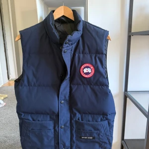 Mörkblå dunväst från Canada Goose - Mycket bra skick. Endast använd ett fåtal gånger. Köpt på NK med kvitto. Pris ny: 7299kr.                   Storlek Xs men passar S mer. Kontakta för mer frågor.