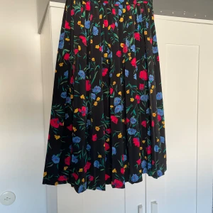 Blommig långkjol från Alfred Dunner - Säljer en svart långkjol från Alfred Dunner med färgglada blommor i rött, blått och gult. Kjolen har plisserad design och resår i midjan för extra komfort. Tillverkad i 100% polyester, perfekt för dig som gillar färg och mönster.