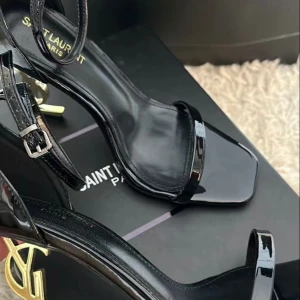 Svarta Saint Laurent sandaler med YSL-klack - Säljer ett par svarta sandaler från Saint Laurent med ikonisk YSL-klack i guld. Skorna har smala remmar, öppen tå och hög klack. Tillverkade i glansigt skinn för en lyxig känsla. Jag skickar med kvitton såklart och deras original kartong samt påsen . Dem ser fortfarande nya ut, har bara haft på mig dem tre gånger 