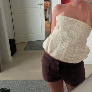 Vit bandeau topp - Säljer en jättefin vit tubtopp med broderade blommor i spets och lätt volang nertill.  Finns en dragkedja i sidan och är perfekt för sommaren💛💛Prislappen finns kvar då den tyvärr är för stor för mig och missade att lämna tillbaka i tid 🙏🏼