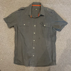 Mörkgrå randig skjorta från Adam -  mörkgrå skjorta från Adam med diskreta tunna ränder, korta ärmar och två bröstfickor. 