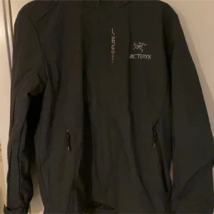 Grå vindjacka från Arc'teryx L - Säljer en svart vindjacka från Arc'teryx i storlek L. Jackan har dragkedja framtill, två sidofickor med dragkedja och meshfoder på insidan. Perfekt för blåsiga dagar och outdoor-äventyr. Snygg minimalistisk design med Arc'teryx-logga på bröstet.