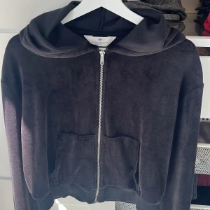 Svart munkjacka med huva från H&M - Mysig svart munkjacka från H&M med dragkedja framtill och två stora fickor. Jackan har huva och ribbade muddar vid ärmslut och nederkant. Perfekt för kyliga dagar när du vill vara både bekväm och stilren. Jättegosig! 