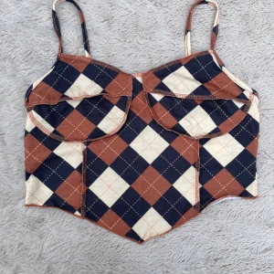 Rutig korsett-topp från SHEIN - Superfin korsett-topp från SHEIN med smala axelband och rutigt mönster i brunt, mörkblått och beige. Toppen har markerade kupor och en spetsig nederkant framtill för en edgy look. Perfekt att styla med jeans eller kjol för en cool vibe.