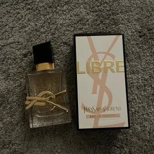 Yves Saint Laurent Libre EdT - Snygg parfymflaska från Yves Saint Laurent, Libre Eau de Toilette. Flaskan är rektangulär i genomskinligt glas med en svart och guldig kork samt en ikonisk guldig YSL-logga runt flaskan. Doften är fräsch och modern, perfekt för dig som gillar lyxiga detaljer. Använd några få gånger, mycket kvar i flaskan (se andra bilden). Hör gärna av dig om du har fler frågor💞