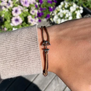 Brunt armband med ankare - Snyggt armband i brunt snöre med ett silverfärgat ankare som lås. Dubbeltrådigt och justerbart, perfekt för en avslappnad och cool stil. Passar dig som gillar marina detaljer och enkel design.