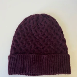 Vinröd stickad mössa med struktur - Mysig vinröd mössa med snyggt stickat strukturmönster och bred ribbad kant.