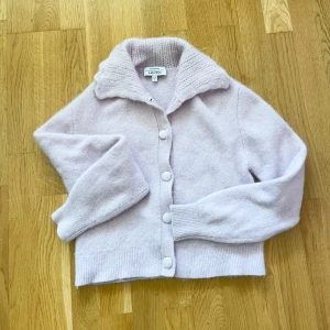 Ljuslila kofta från & Other Stories - Supermjuk och fluffig ljuslila kofta från & Other Stories Paris Atelier. Koftan har stora knappar framtill, bred ribbad krage och långa ärmar. Perfekt för lager-på-lager och ger en chill men ändå söt vibe. Materialet är stickat och känns riktigt cozy.