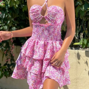 Rosa blommig volangklänning - Supersöt kort klänning med rosa och vita blommor, volanger i flera lager och smockad midja. Omlott-detalj framtill med cut-out och halterneck. Perfekt för sommardagar när du vill sticka ut lite extra. Köpt på shein, är oanvänd! 