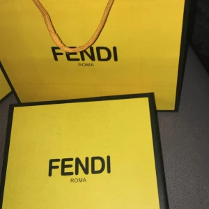 Fendi bälte med FF-logo - Säljer ett snyggt Fendi bälte med klassisk FF-logo i svart metall. Bältet har ett mönstrat band i grått och svart och levereras i originalförpackning. Perfekt accessoar för att lyfta din outfit.