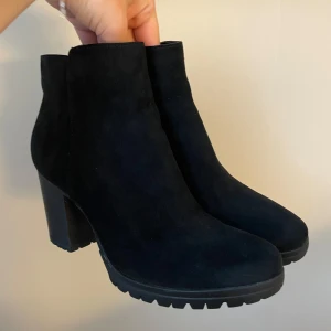 Svarta stövletter från Graceland - Aldrig använda! Snygga svarta stövletter från Graceland i mockaimitation med chunky klack och grov sula. Dragkedja på sidan gör dem enkla att ta på. Perfekta till både jeans och kjol för en cool look.