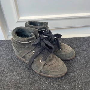 Grå mockasneakers Isabel Marant - Snygga grå sneakers från Isabel Marant i mjuk mocka med dekorativa perforeringar och sicksack-detaljer. Skorna har svarta snören och platt sula, perfekt för en cool och avslappnad look.