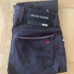Svarta jeans från Jacob Cohën Limited edition  - Snygga svarta jeans från Jacob Cohën BARD Ltd med exklusiva detaljer som röd brodyr och selvedge-kant. Klassisk femficksmodell med knappar framtill och diskreta kontrastsömmar. Jeansen har en stilren look och är tillverkade i mjukt bomullstyg.   Även verifierade av vestiaire collective