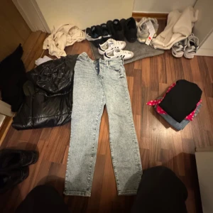 Acid wash mom jeans från &Denim - Säljer ett par ljusblå mom jeans från &Denim med ultra hög midja och klassisk knappgylf. Jeansen har en rak passform och cool acid wash-look som ger en retro vibe. Perfekta för dig som gillar vintagekänsla och relaxed stil.