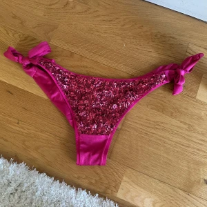 Rosa bikiniunderdel med paljetter från Calzedonia  - Snygg bikiniunderdel i stark rosa färg från Calzedonia. Nyköpt med lapparna kvar, men tyvärr tog jag av den före jag testade…🙈och de passade tyvärr inte. Framsidan är täckt av glittriga paljetter och sidorna har knytband för en justerbar passform. Materialet är glansigt och känns lyxigt, perfekt för strandhäng eller poolparty. Köpt för ungefär 450 kr och säljer för 300 då den är helt ny och aldrig använd, endast testad, skriv privat för fler frågor💗