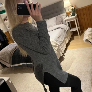 Grå ribbstickad lång tröja med slits - Mysig grå långärmad tröja i ribbstickat material med slitsar på sidorna. Tröjan har en rak och loose passform, rund halsringning och är perfekt att styla med leggings eller jeans. Enkel och stilren look som funkar året runt.