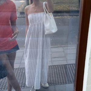 Vit långrandig sommarklänning - Luftig långklänning med ränder och smala axelband. Klänningen har rak överdel och faller snyggt från bysten ner till anklarna. Perfekt för varma dagar och enkel att styla med sneakers eller sandaler.