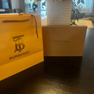 Burberry rutigt skärp med guldspänne - Exklusivt Burberry-bälte i klassiskt beige och svart rutigt mönster med ikoniskt guldigt B-spänne. Tillverkat i äkta kalvskinn och levereras i originalförpackning. Perfekt accessoar för att lyfta din outfit med lyxig känsla och tidlös design.